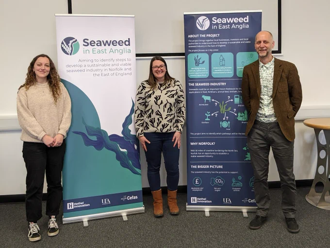 Three people stoof smiling at the camera in front of two information banners
