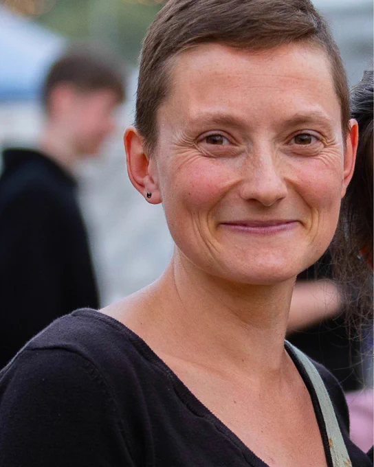 Anna Fischer has short dark hair. They are smiling looking at the camera. 