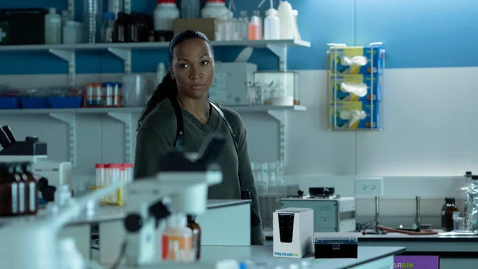 Agent Navarro investigating the TSALAL Arctic Research facility, looking  disappointedly at all of the single-use plastics before she sees the low-carbon pipette tips and glove recycling bin.