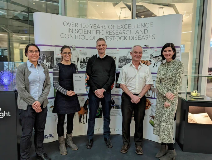 Five people smiling stood in front of a large white poster. One is holding a certificate