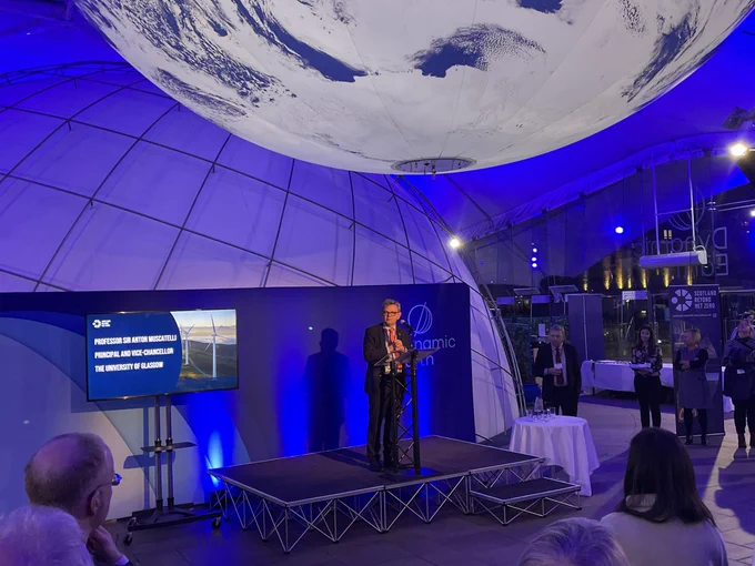 Professor Sir Anton Muscatelli standing at podium in front of crowd with large globe hanging from ceiling.