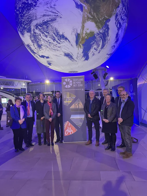 Group of people standing with banner, globe hanging from ceiling.