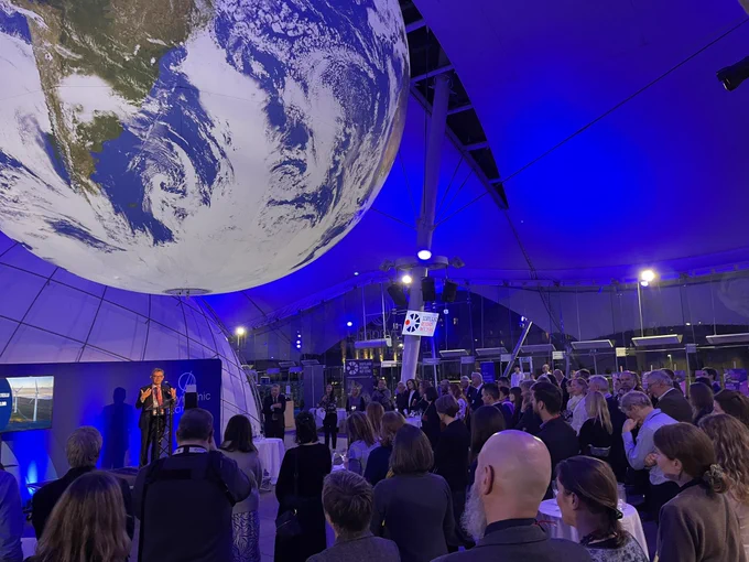 Professor Sir Anton Muscatelli standing at podium in front of crowd with large globe hanging from ceiling.