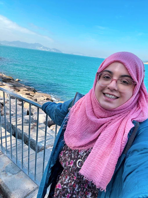 A photo of Fatima smiling by the water from her PTO during new years on Cheung Chau island in Hong Kong. Behind her are the beautiful blue waters of the South China Sea. 
