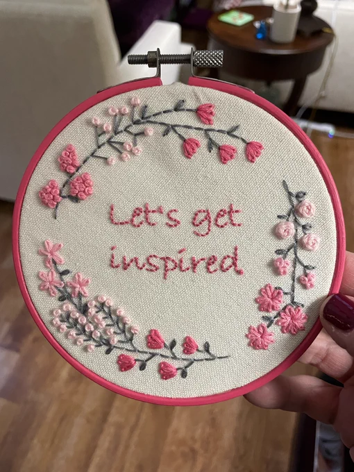 Embroidered print that says "Let's get inspired" surrounded by pink flowers