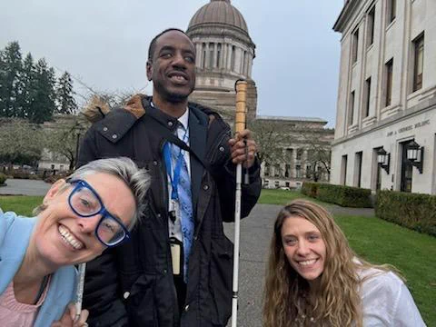 A man with a white cane and two women  in front of the Washington State capital building 