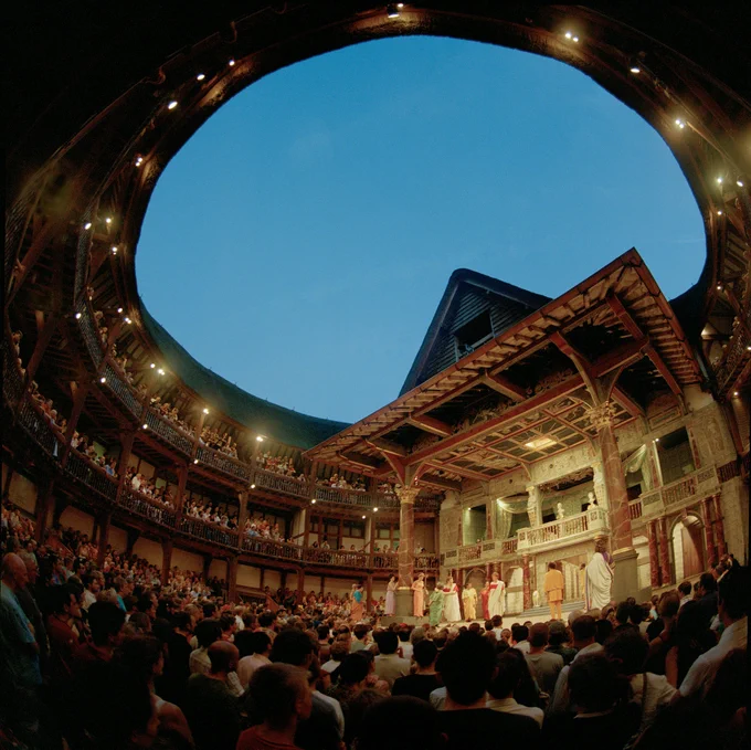 A view from the back of the Yard in the Globe Theatre at night time - the audience watching on as actors bow onstage.