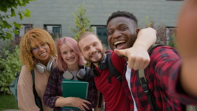 Four teens at school embracing and taking a selfie.