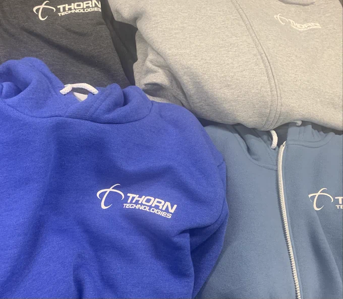 Hooded sweatshirts in shades of blue and gray with the Thorn Technologies logo on them. 