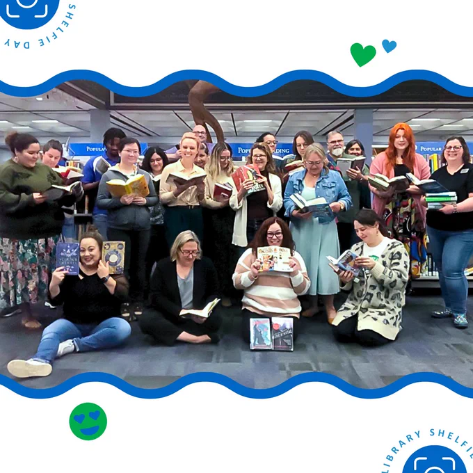 Group of library employees smiling and holding books in front of Popular Reading collection shelves in Bell Library.