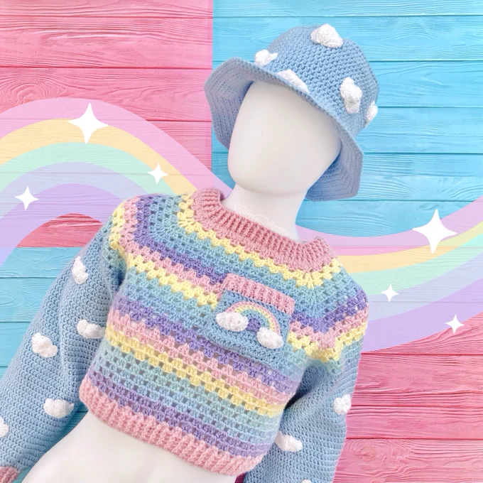 A bright white mannequin wearing a light blue crochet bucket hat with white cloud print and a cropped pastel rainbow striped crochet sweater with a rainbow and cloud chest pocket and blue sleeves with a cloud pattern on them