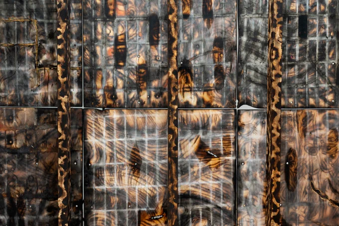 A mottled black, brown, tan and white artwork, featuring burnt patterns, a grid made of chalk tracings, and linseed oil patches. the work showed six of 8 square 'panels', attached to two-by fours treated in the same way.