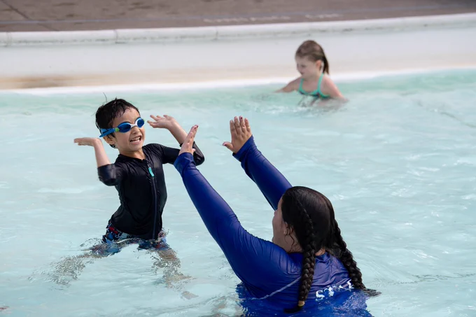 Child high-fiving a swim instructor in a pool.