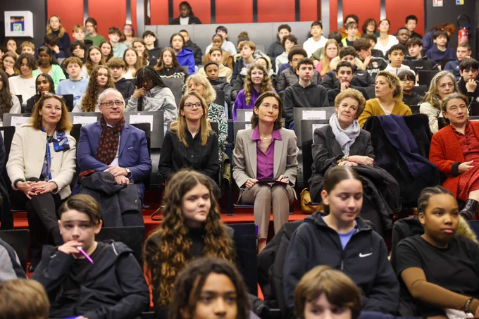 Dans un amphithéâtre, des collégiens sont assis sur les deux premiers rangs. Amélie Oudéa-Castera et Aurore Bergé, ministre déléguée chargée de l’Égalité entre les femmes et les hommes et de la Lutte contre les discriminations, sont au 3ème rang. Derrière eux, des collégiens occupent les rangs du fond.