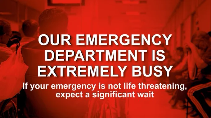 People sitting in a crowded A&E waiting room. Text: our emergency department is extremely busy. If your emergency is not life threatening, expect a significant wait.