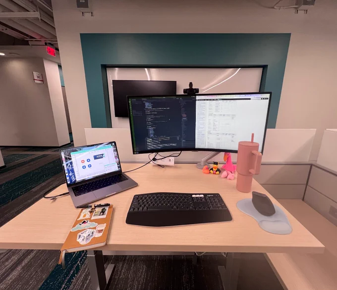 Laylas desk at Oracle HQ, in standing mode, with an ultra wide monitor and a MacBook on the desk.