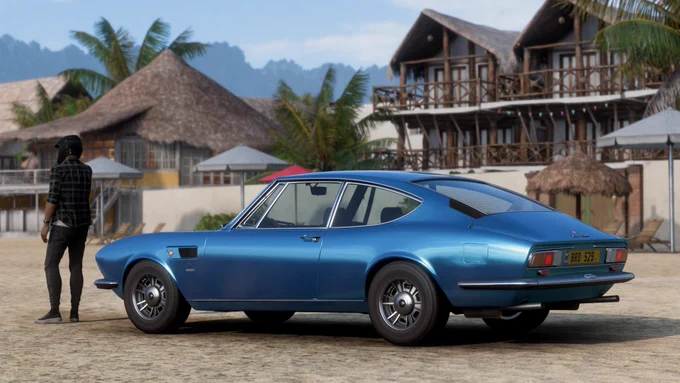 A 1969 Fiat Dino 2.4 Coupe finished in an early rendition of my replicated Azzuro Met. along the beachfront houses of Playa Azul in Forza Horizon 5.