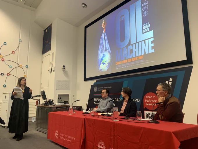 Panel sitting in front of a big screen saying 'The Oil Machine'