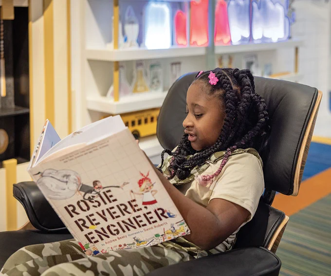 An image of a girl reading "Rosie Revere Engineer" in The Questioneers exhibit.