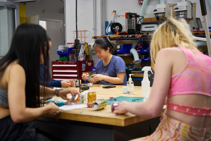 Four students are gathered around a table in a makerspace, working on projects together. 