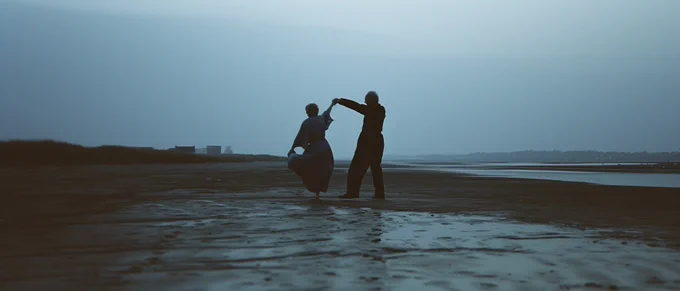 Cinematic still of [an elderly couple] [dancing] [on an empty beach] [in the early morning]. Minimalist gothic ambiance, enigmatic, rollerwave aesthetic, urban earthworks backdrop. Captured on Kodak Ektar 100, soft lighting, low key contrasts, film grain, wide angle --ar 21:9 --v 6