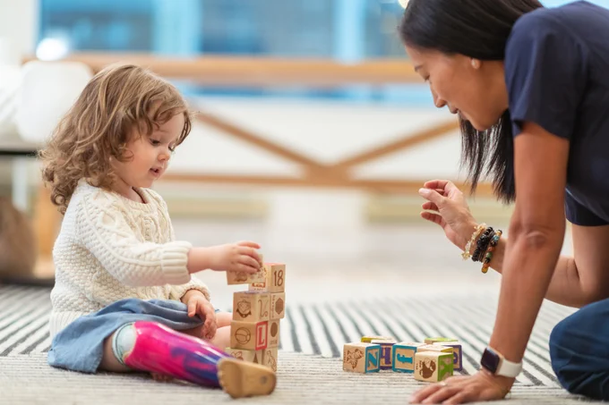 A woman and child with a prosthetic leg happily playing with colorful blocks on the floor