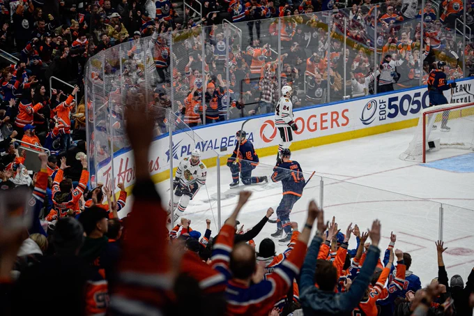 Zach Hyman celebrates a goal in an Oilers uniform. There are fans cheering in the foreground. 