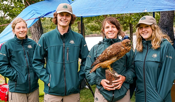 Four Parks Canada staff pose with a taxidermy bird of prey. 