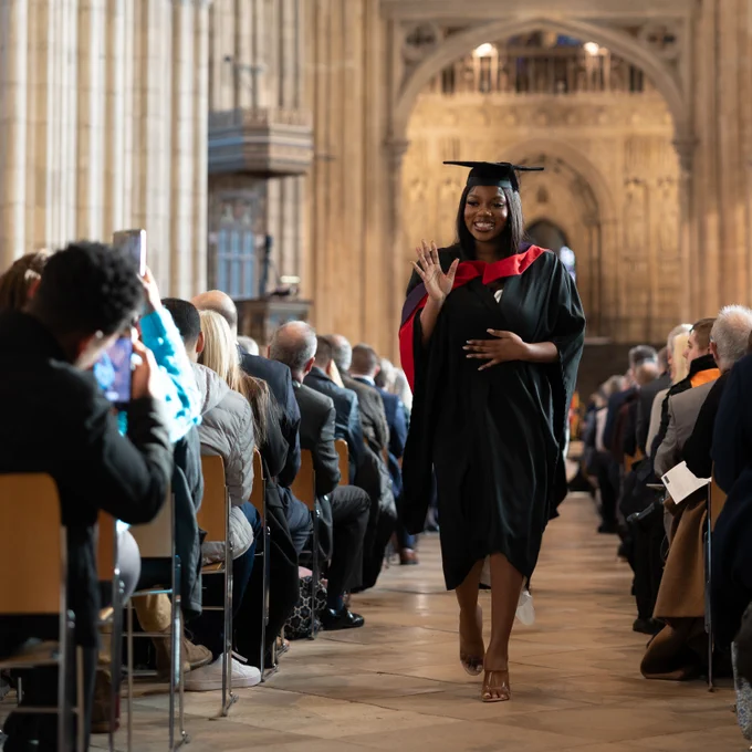 Photo of a graduate waving while walking down the aisle