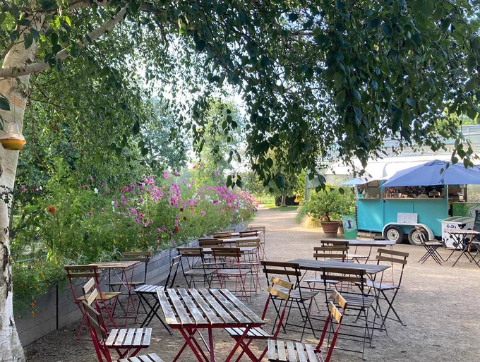 Jericho Coffee's light blue truck is in the background, next to the river. There are tables and chairs in the foreground.