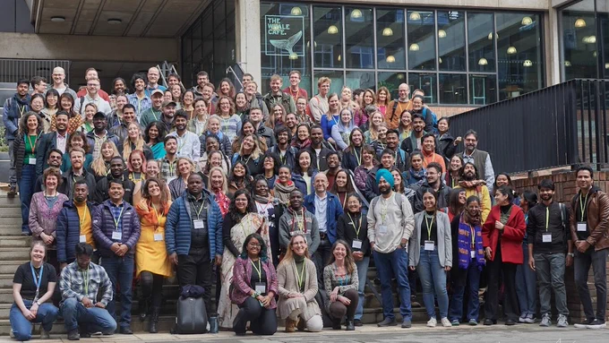 Picture of happy delegates at the SCCS conference in front of the David Attenborough Building. The Whale Café peeps over the top in the background. There are some black railings on the right hand side of the photo (stage left). People are wearing lanyards of various colours - the reasons for this are unknown, but rumored to be vitally important. Some people are wearing glasses, others are not. 