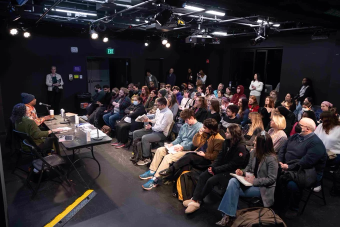 Dozens of people sit and listen to a presentation.