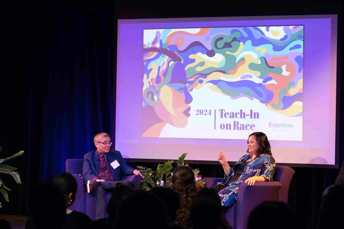 Two people sit on a stage and converse.