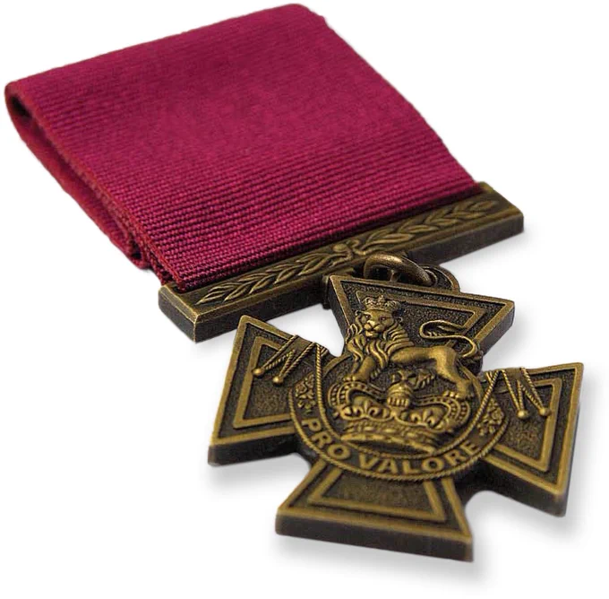 Closeup of the British Victoria Cross. It is of bronze colour, matte in finish, with a plain crimson ribbon. Text on the cross: “Pro Valore”.