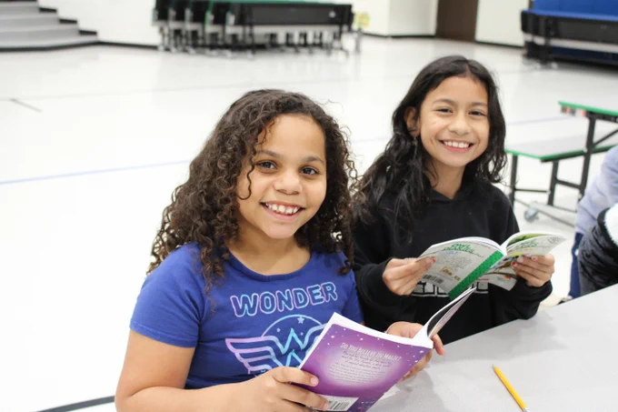 Image of two girls looking up smiling while holding the books they are reading