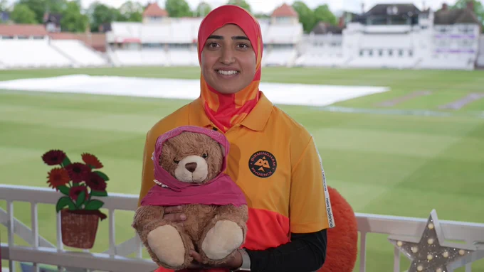  Abtaha Maqsood holds a bear wearing a hijab with a Trent Bridge cricket ground in the background