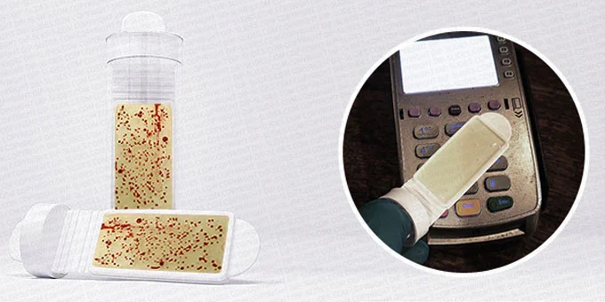 Bacteria testing dipslide covered in red bacteria dots and a chip and pin machine being tested.