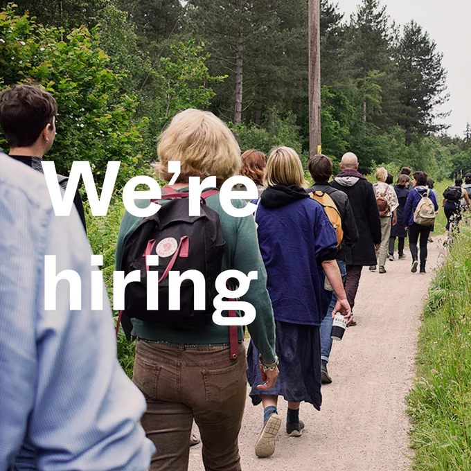 The text, 'We're hiring', overlaid on an image of a group of people walking away down a path between green trees and plants. 