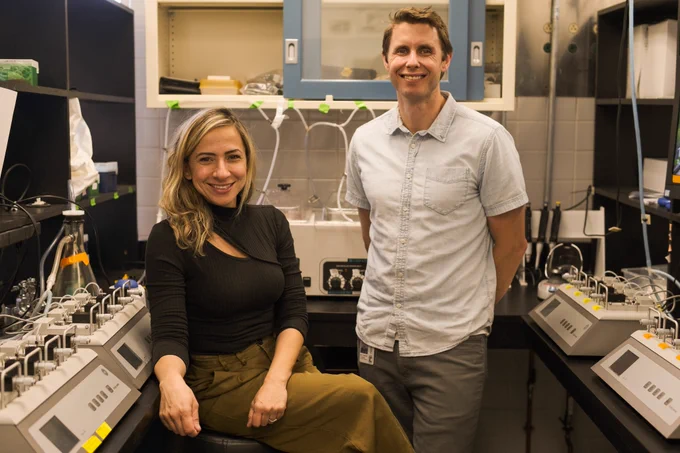 USC cardiovascular researchers Camilla Wenceslau (left) and Cameron McCarthy (right) pose, smiling, for a photo in their laboratory. They are flanked on both sides by research equipment on black lab tables. 
