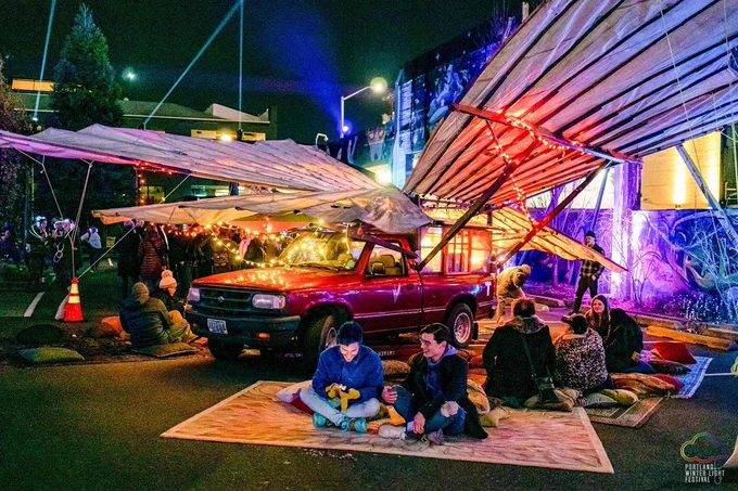 T-Horse, the truck with a mobile teahouse and giant wings, adorned with colored lights and people sitting around it on carpets enjoying tea and conversation.