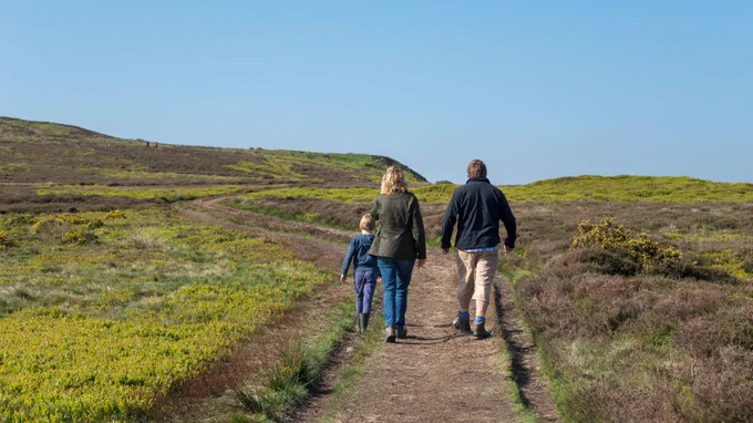 Photo that shows the back of a family walking up towards the top of a hill along a path.