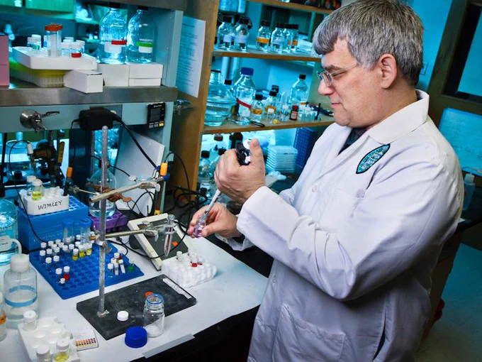 Bill Wimley wears a white coat while working with research equipment in a lab.
