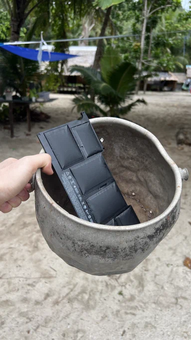 Swollen MacBook Air battery in a thin beat-up metal pot amidst a beach background.