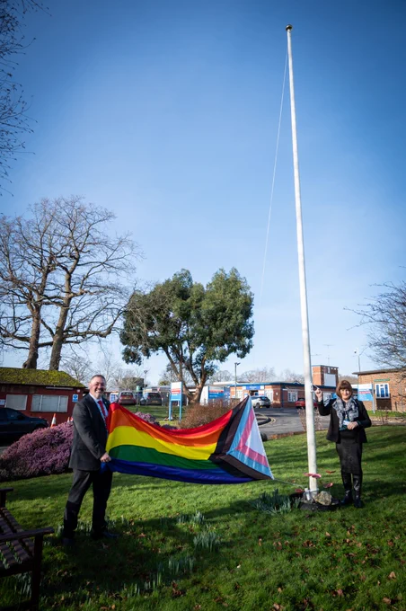 Two members of the QVH executive team hoisting a Progress pride flag onto the flag pole. 