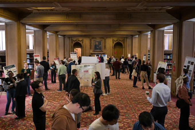 A large group of people walks around a library looking at research posters.