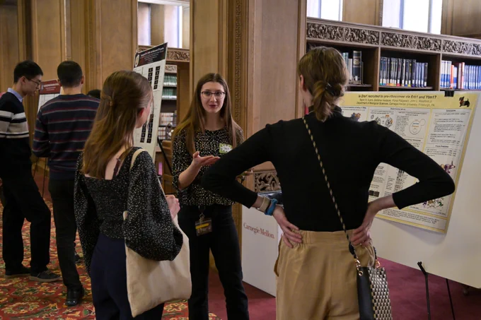 A woman tells two other women about her research in front of a poster.