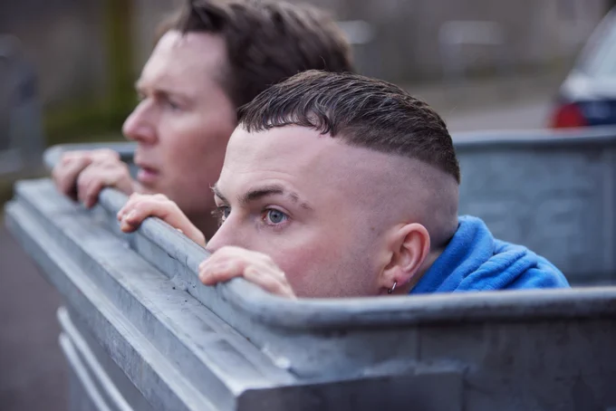 Photo of Billy Murphy (Shane Casey) and Conor MacSweeney (Alex Murphy) peering out from inside a rubbish bin in The Young Offenders Season 4
