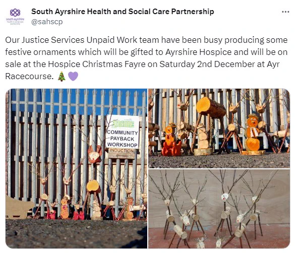 Snowmen and reindeer of various sizes made of sticks, corks and wood. They're lined up outside a fence and a sign that says 'Community Payback Workshop'