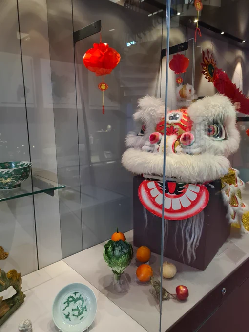 Glass case with pottery, paper decorations, fruit and vegetable and traditional lion dance costume.