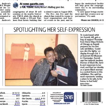 Two black women embrace in front of a large snapshot of a little girl in pajamas. Caption is:  St. Louis-based artist Jen Everett, left, gets a hug of support Thursday from friend Maya Roberts of Chicago as Everett prepares for her first solo exhibition, ‘Could you dim the lights,’ on display through Oct. 5 at Krannert Art Museum in Champaign. Everett says her artwork involves themes of Black life, family and responses to turmoil, and that her identity as a queer Black woman is a central theme in this exhibition. She said her work represents ‘seeking a place to be safe, to be home, to feel held.’